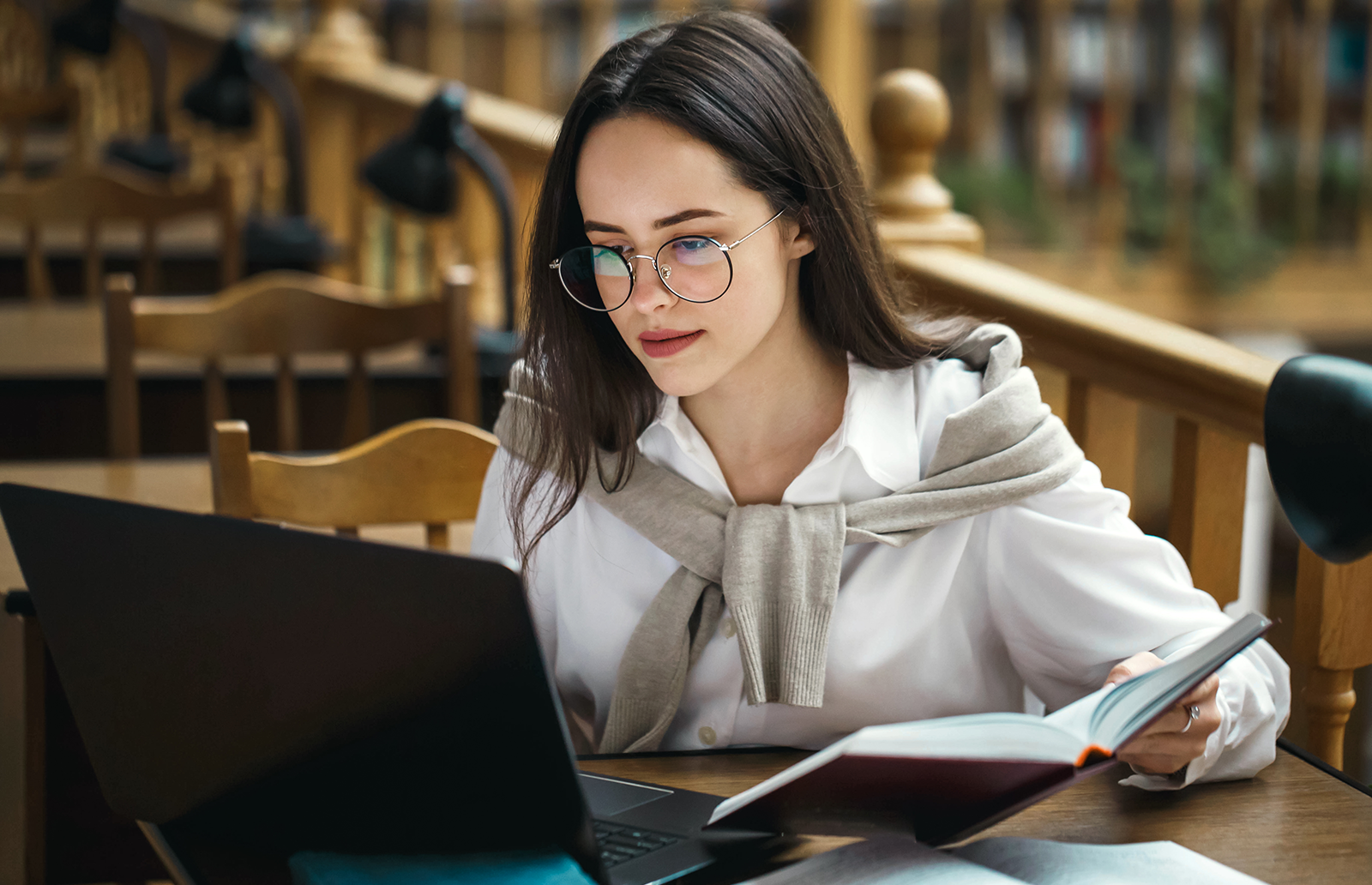 Young woman holding a book while working on a laptop in a study area