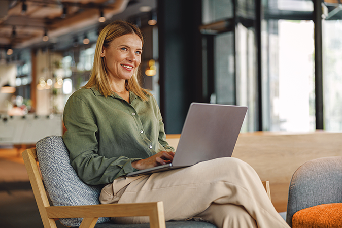 Young woman smile while sitting in a chair with a laptop on her lap