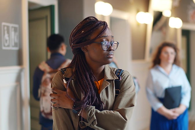 Young woman hugging herself looking very anxious in a university hallway