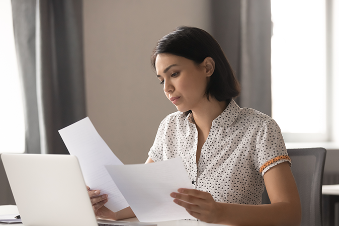 Young woman looking at documents sitting at a desk in front of a laptop