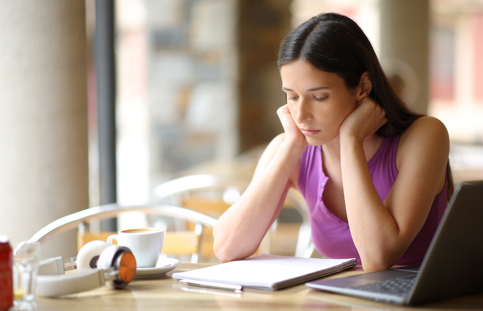 Young woman sitting at a table reviewing notes with a laptop and headphones nearby