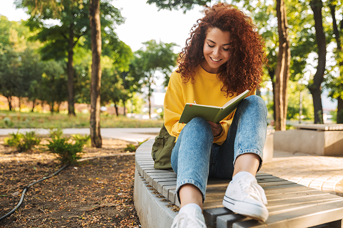 Young woman sitting outside reading a book