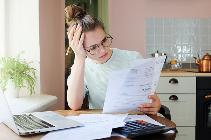 Young woman sitting at a table holding financials with a laptop and calculator looking sad