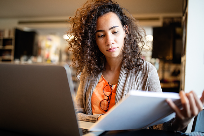 Young woman reading a textbook in front of a laptop in a library