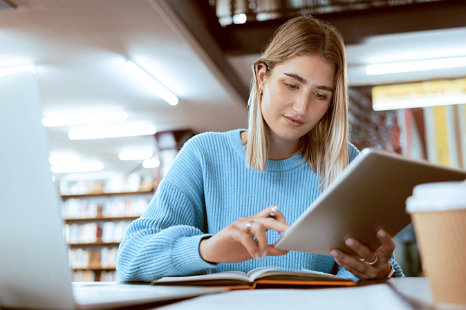 Young woman in the library studying on a laptop and a tablet