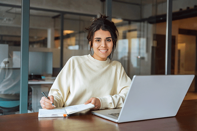 Young woman writing notes in front of a laptop