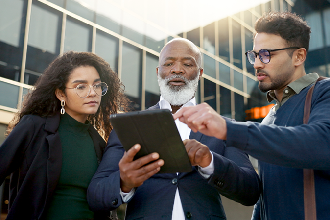 Three businesspeople looking at tablet outside corporate office building