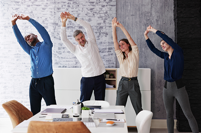 Four business coworkers stretching in the meeting room