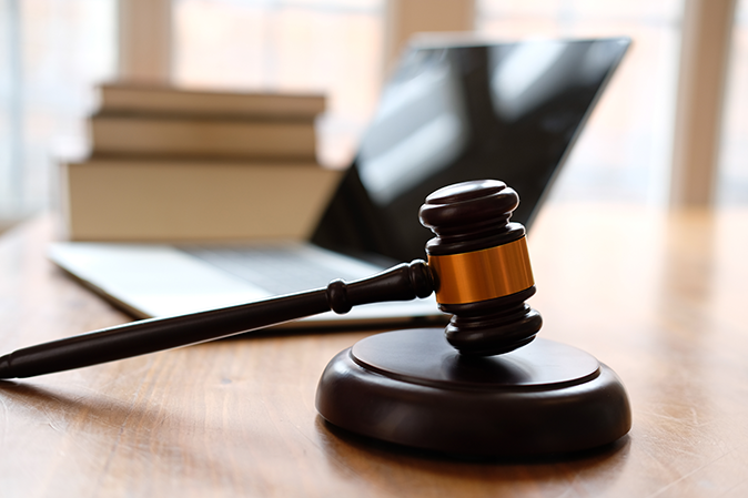 Judge's gavel sitting on a desk in front of a laptop and books