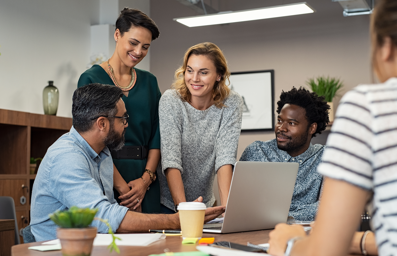 Group of men and women in an office discussing a project in front of a laptop