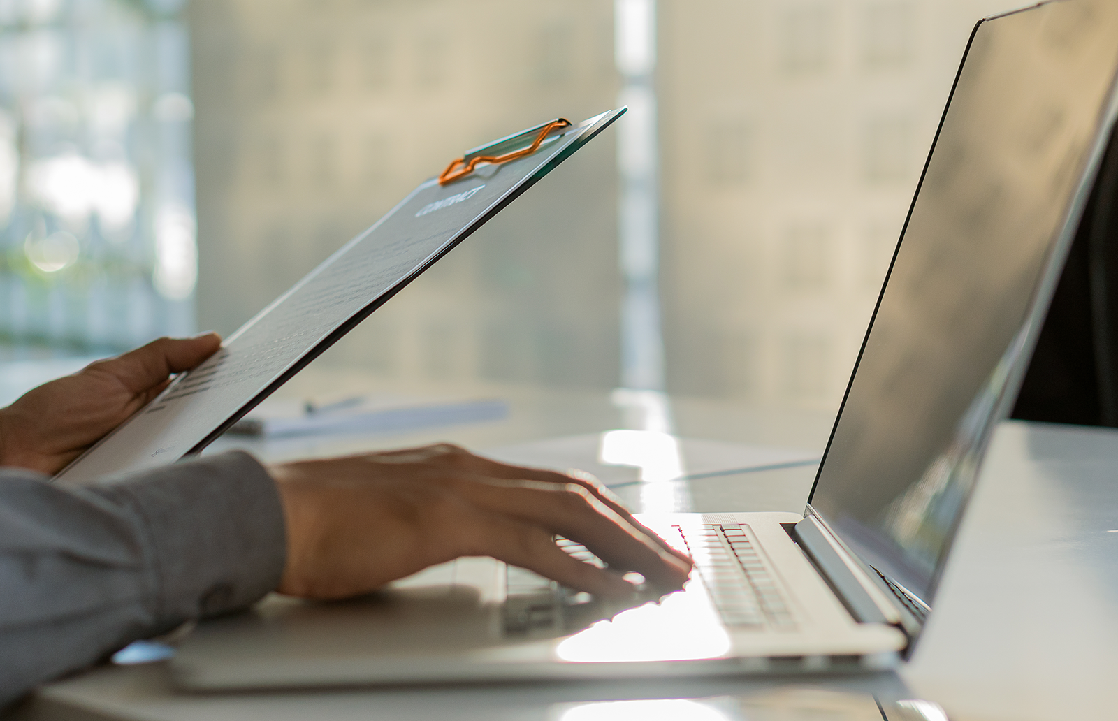 Man holding a clipboard while typing on a laptop