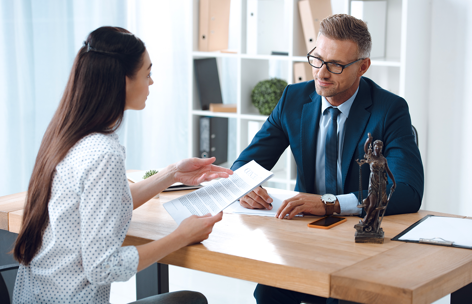Young male lawyer discussing documents with a client sitting at desk in an office