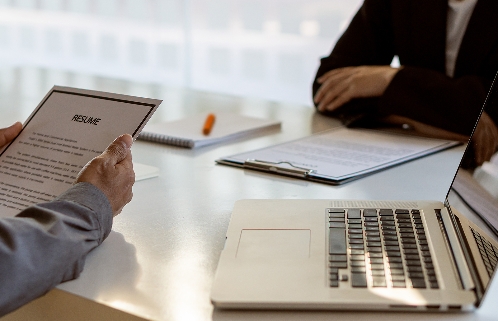 Man reviewing a resume in front of a laptop while interviewing someone
