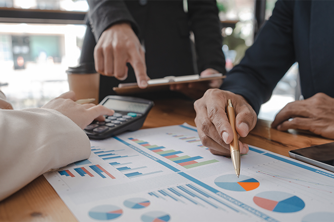 Three business people point, reviewing, and calculating reports