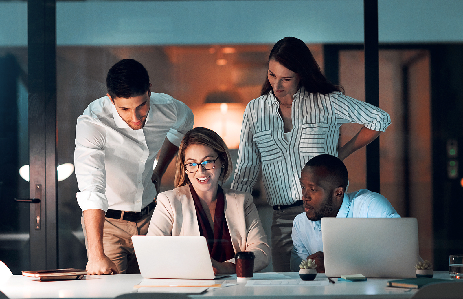 Four professional in an office in front of a couple laptops working together on a project