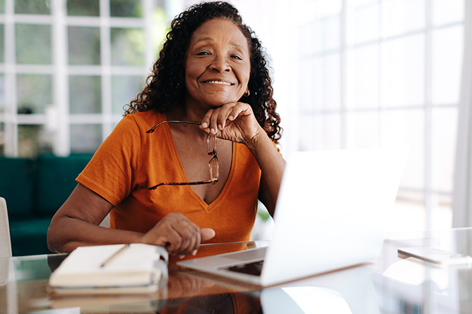 Senior woman managing her business from her home office, using a laptop to work with clients and employees remotely. Experienced woman showing her ability to adapt and thrive in a hybrid business world.