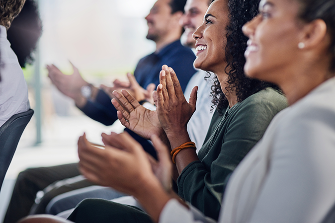 Group of professionals smiling and clapping at a conference