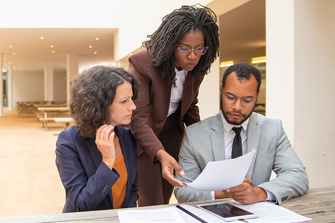 Three professionals looking over documents together at a table with a tablet and more documents