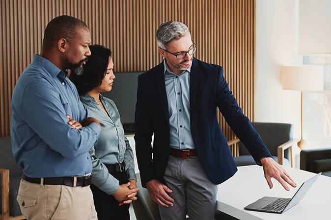 Three professionals in an office looking at a laptop