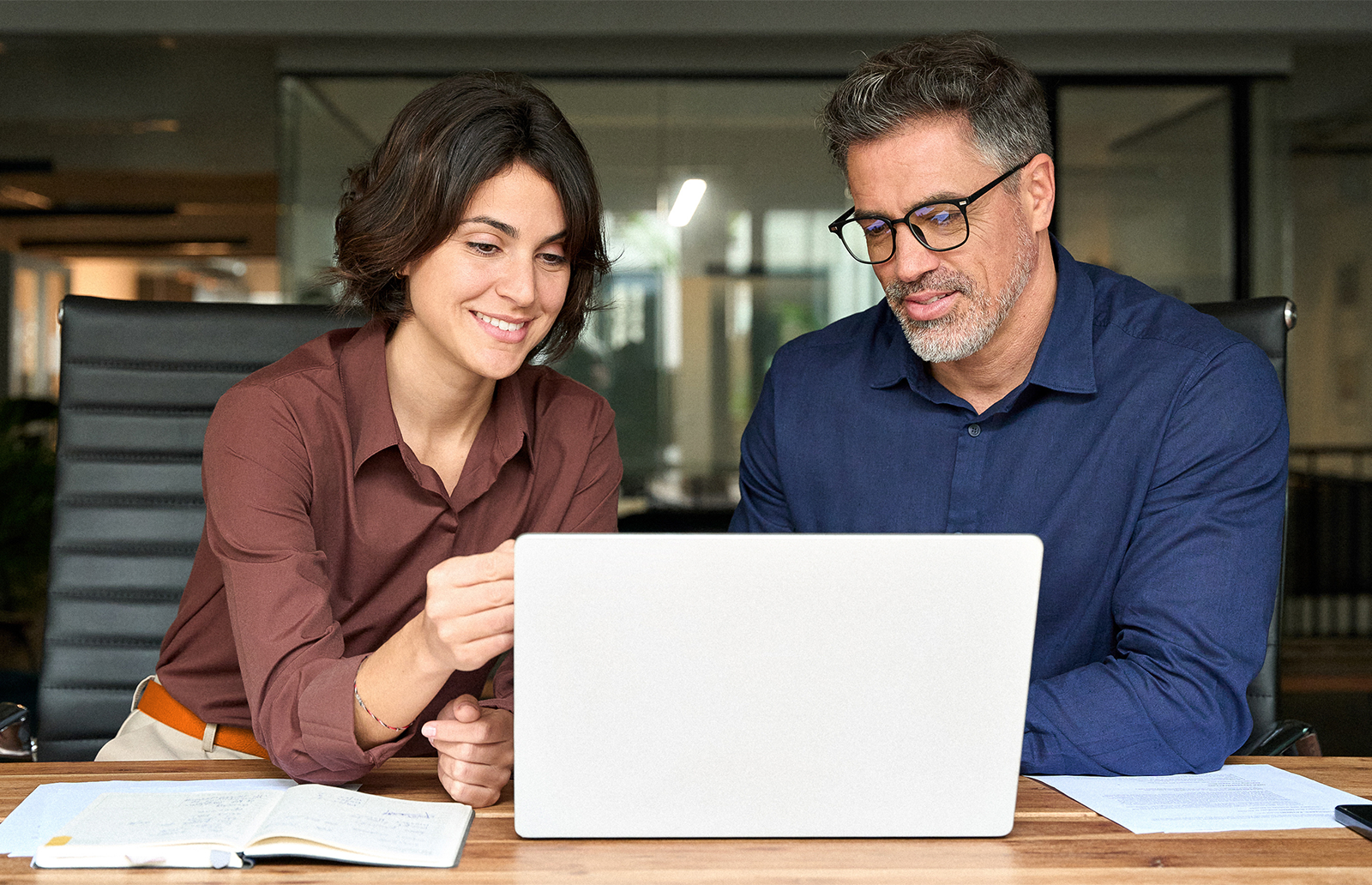 Young woman professional working on a laptop with a middle-aged man in an office setting