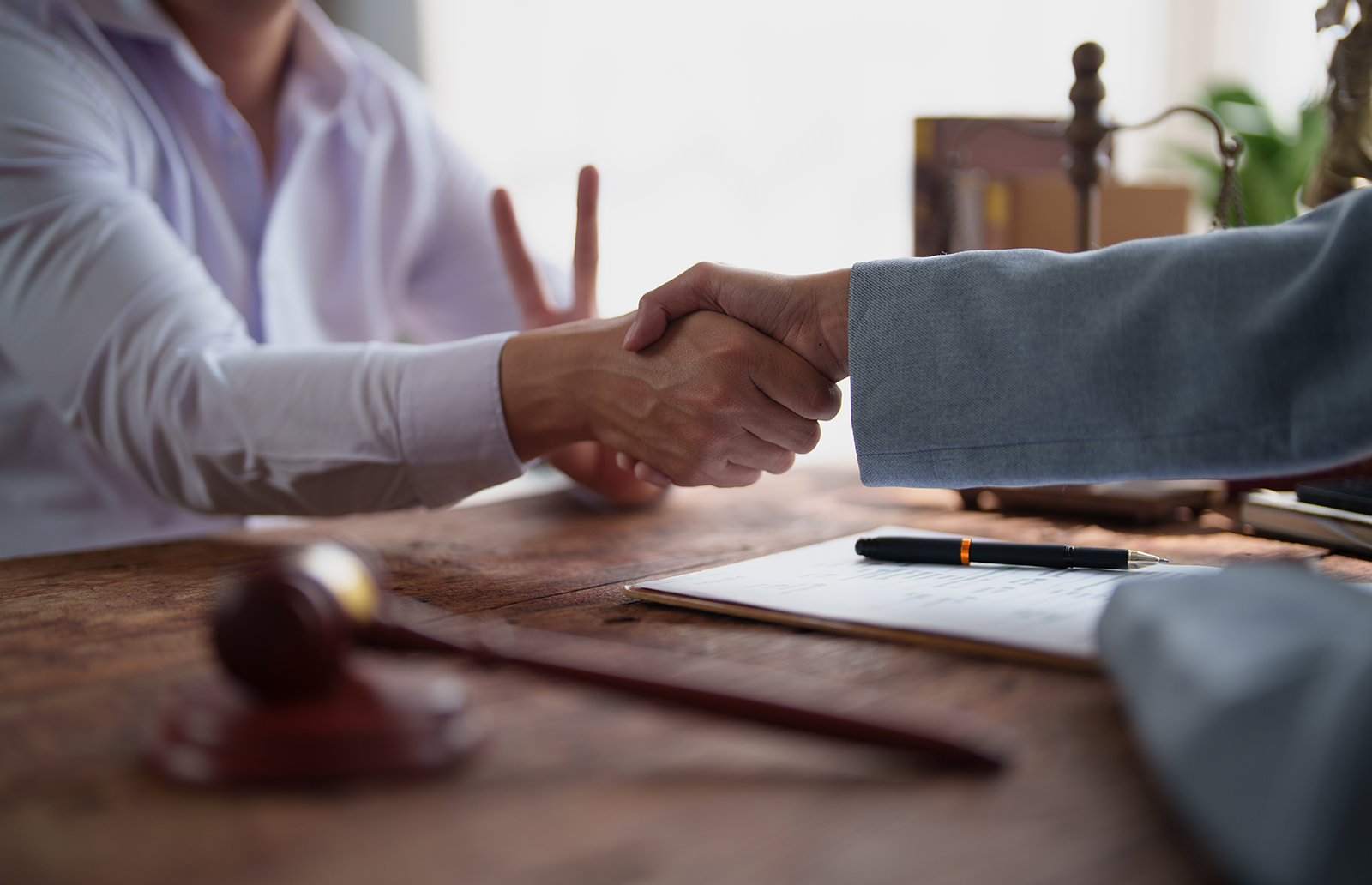 Two professionals shaking hands while sitting at desk with a judge's gavel