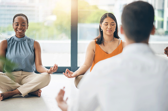Two professional women meditating in a class with another man and others