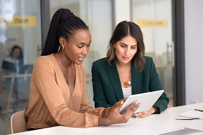 Two professional women in an office working on a tablet together