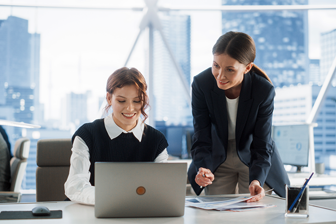 Two young woman professionals working on a project in front of a laptop in an office