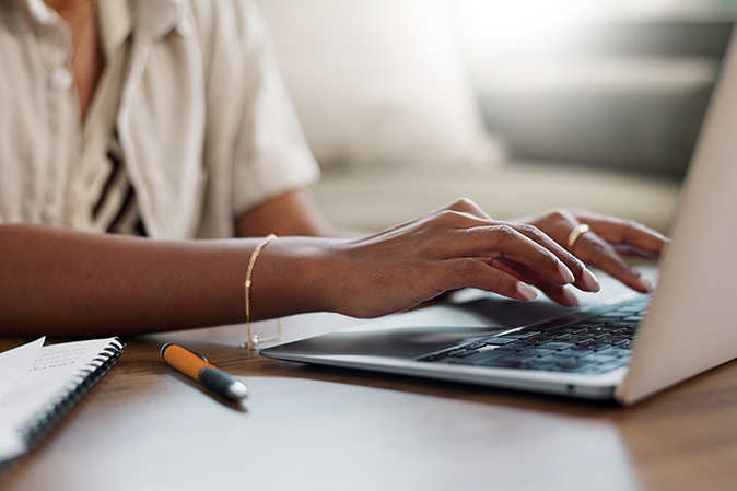 Woman typing on laptop with a notepad and pen nearby