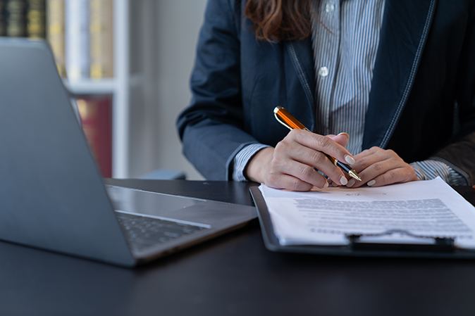 Young woman professional sitting in front of a laptop with a pen and document on a clipboard