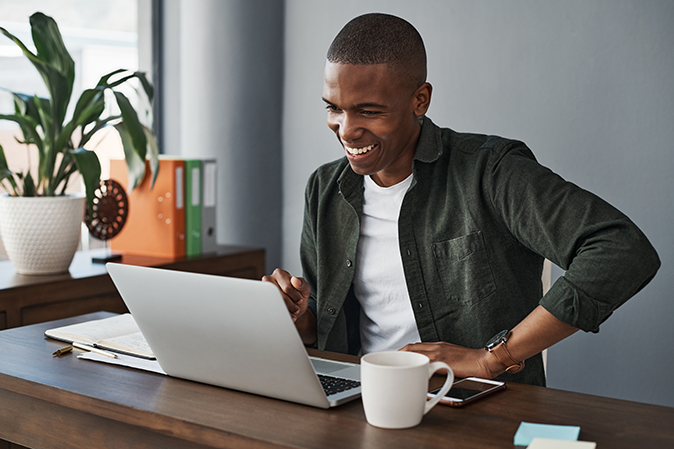 Young man smiling in front of a laptop with a cup of coffee in a home office