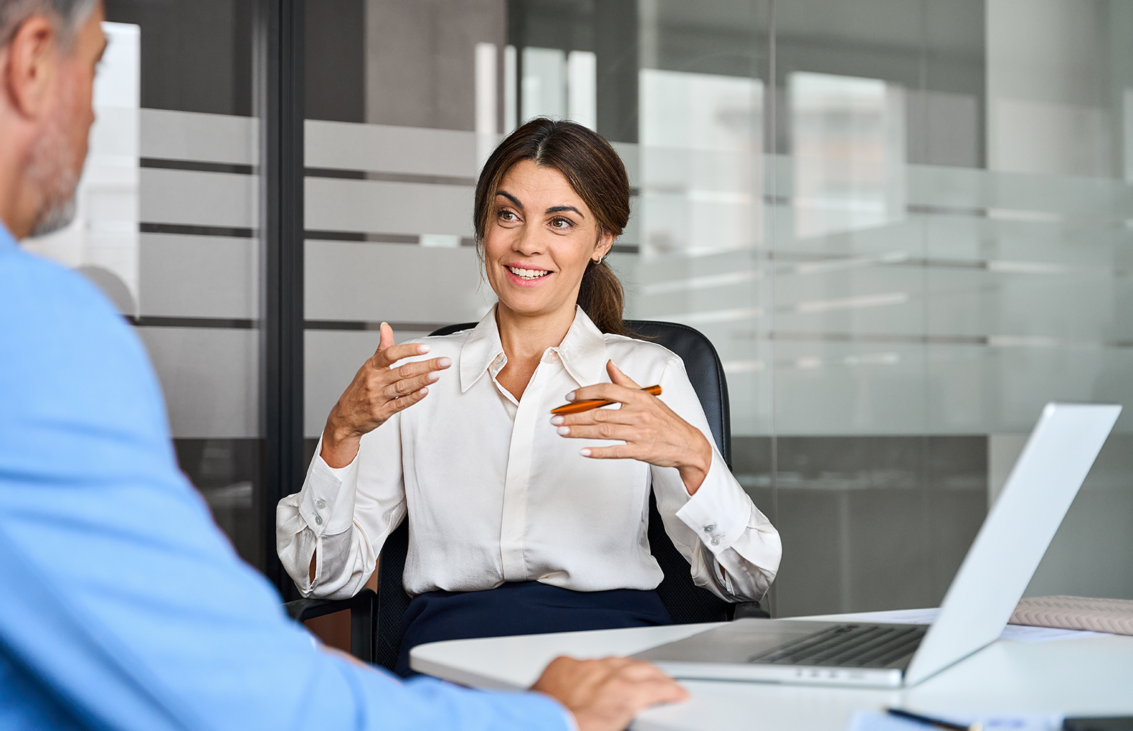 Young woman explaining something to another man sitting in an office in front of a laptop
