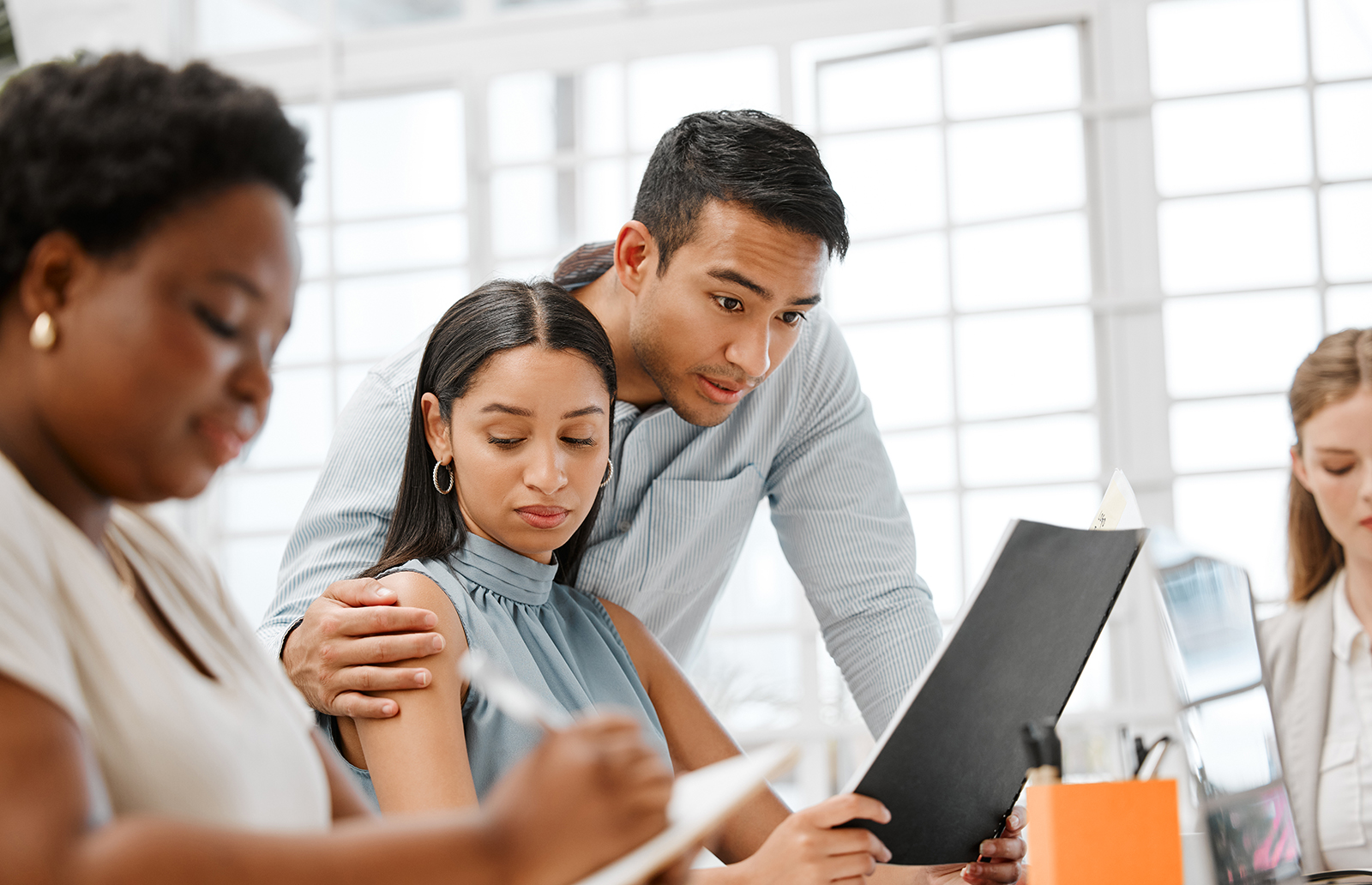 Young woman in an office looking at the hand of a male coworker that is on her shoulder
