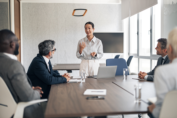 Young professional woman presenting to a team of men and woman at a conference table in an office building