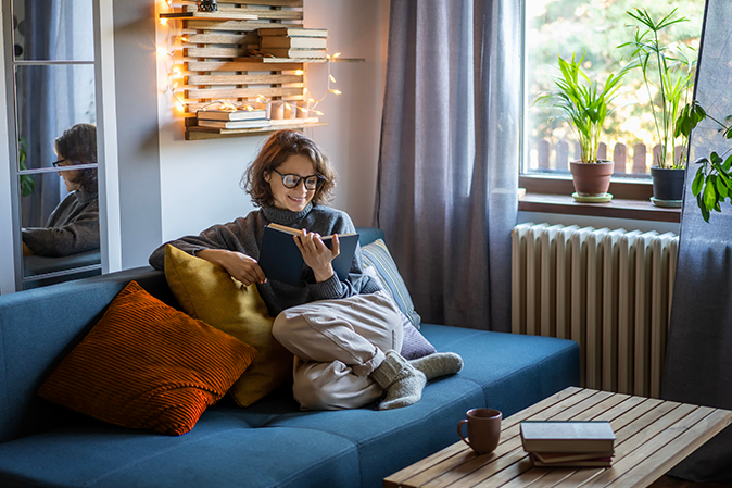Young woman reading a book curled up on a couch in her living room