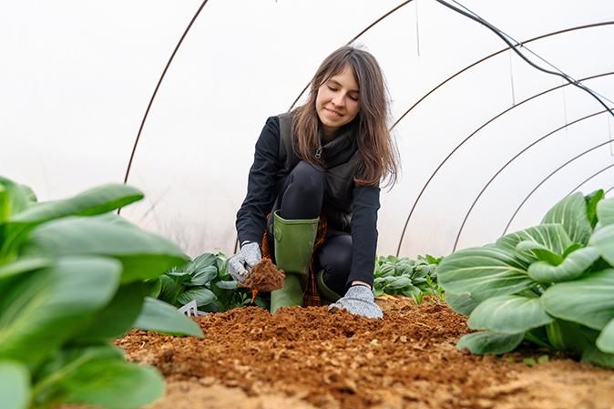 Young woman scooping soil inside a greenhouse cultivating plants