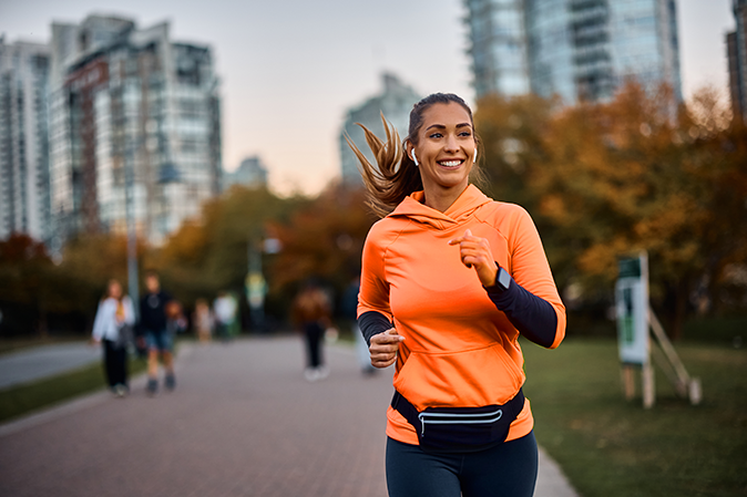 Young woman wearing ear buds while running through a park
