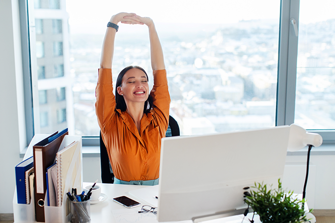 Young woman smiling while stretching in an office in front of a computer
