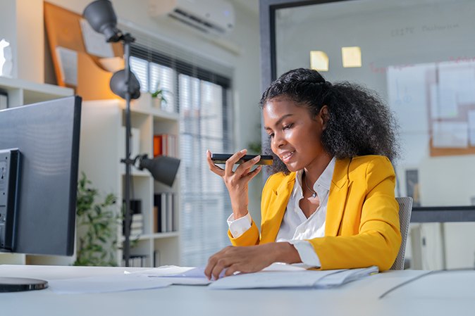 Young woman talking into mobile device while going over documents in front of a computer
