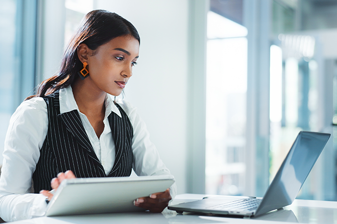 Young woman professional typing on a tablet while watching something on a laptop