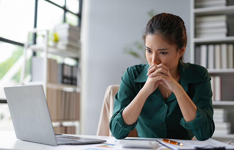 Young businesswoman is holding her hands together in front of her mouth, looking worried while working at her desk