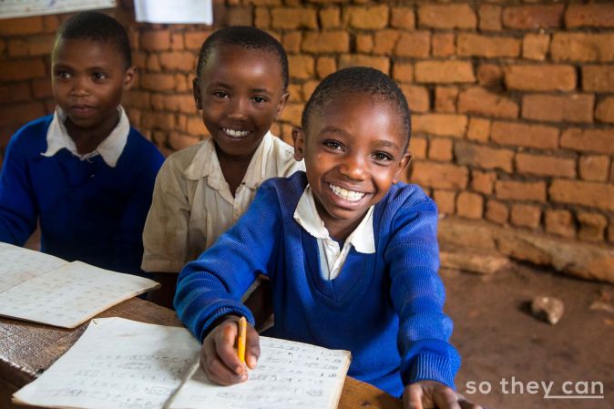 Three smiling school girls in classroom in Kenia, photo supplied by So They Can