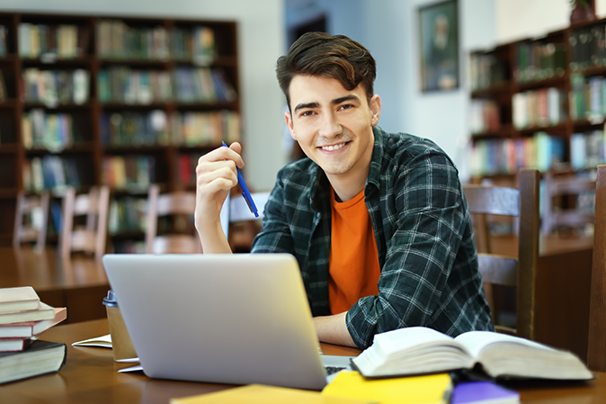Young man studying in the library on his laptop