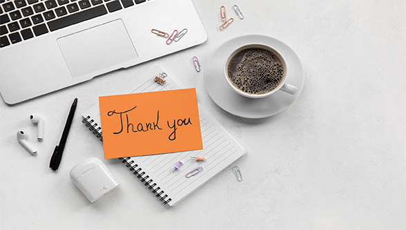 Thank you note sitting on a notepad with a cup of coffee in front of a laptop