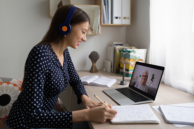 Young woman taking notes while working with a virtual tutor