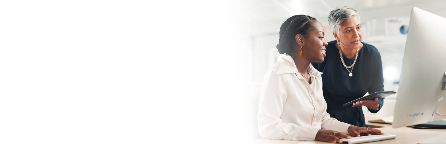 Woman professor looking over the shoulder of a young woman working on a computer