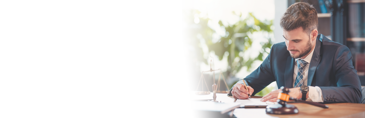 Young man wearing a business suit taking notes with a judge's gavel and the scales of justice sitting on the desk