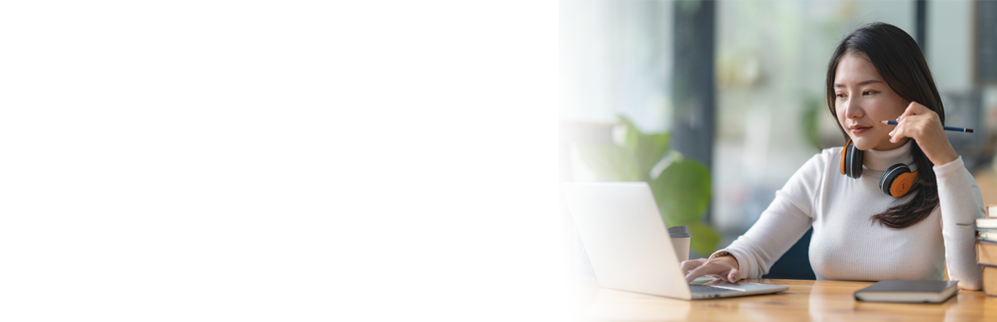 Young woman with headphones around her neck, holding a pencil while working on a laptop