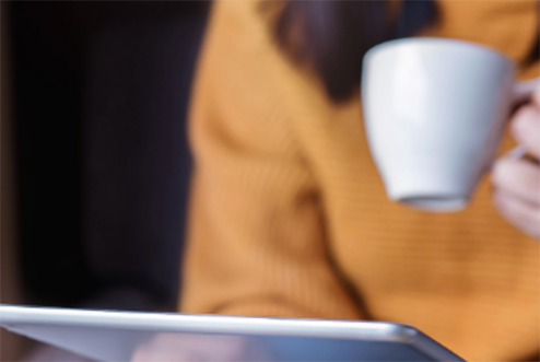 Person holding a cup while on a tablet