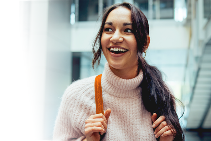 Young woman smiling on a college campus wearing a backpack.